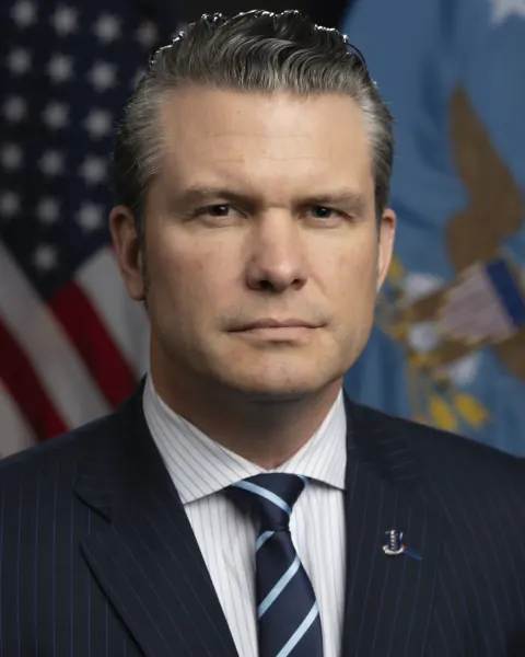 Official 2025 portrait of Pete Hegseth in a dark suit before United States and Defense Department flags.